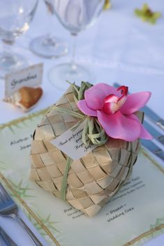 a pink flower sitting on top of a table next to wine glasses and utensils