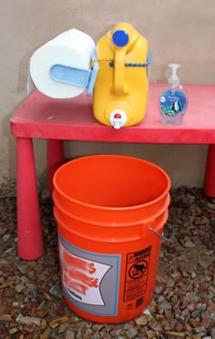 an orange bucket sitting on top of a red table next to a white and blue container