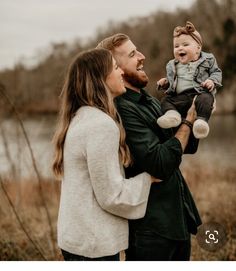 a man holding a baby while standing next to a woman in front of a body of water