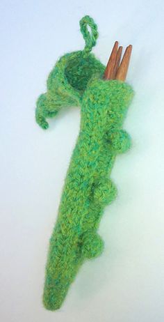 a green crocheted alligator ornament hanging on a white wall with two wooden sticks