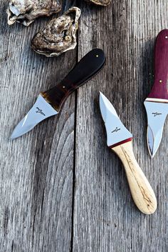 three different types of knives sitting on top of a wooden table next to oysters