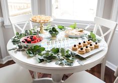 a white table topped with desserts and plates filled with fruit on top of it