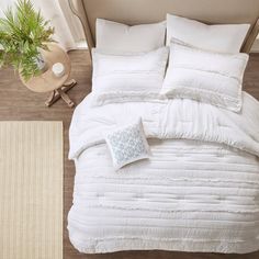 an overhead view of a bed with white comforter and pillows on the floor next to a potted plant