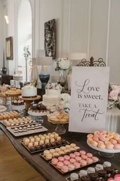 a table topped with lots of different types of cakes and cupcakes next to a sign that says love is sweet, take a treat