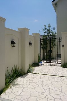 a white gated driveway leading to a house with plants growing on the fence posts