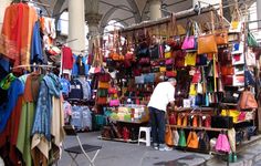 a man standing in front of a display of handbags and purses at an outdoor market