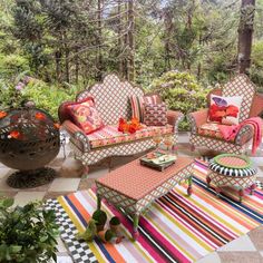 an outdoor patio with striped rugs and colorful furniture in the foreground, surrounded by trees