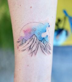 a watercolor tattoo on the leg of a woman with mountains and stars in the sky