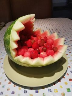 a watermelon cut in half with grapes and raspberries inside it on a plate