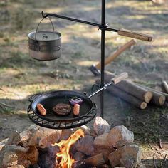 a grill with hot dogs cooking on top of it next to logs and fire pit