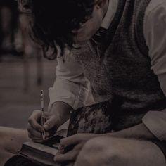 a man sitting down writing on a piece of paper with a pen in his hand