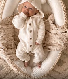 a baby in a white outfit laying on top of a blanket and wearing a hat