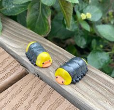 two small yellow and black toy animals sitting on top of a wooden bench next to green leaves