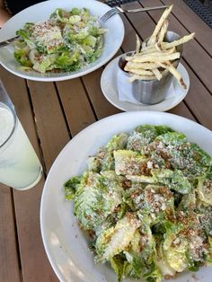 two white plates filled with salad and french fries on a table next to a glass of milk