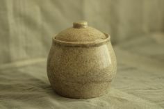 a brown ceramic jar sitting on top of a white sheeted tablecloth with a light colored background