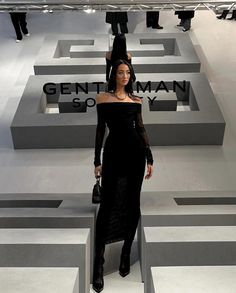 a woman standing in front of a maze with her hand on her head, wearing a black dress