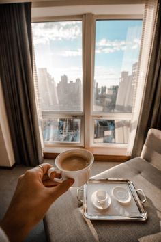 a person holding a cup of coffee in front of a window with cityscape