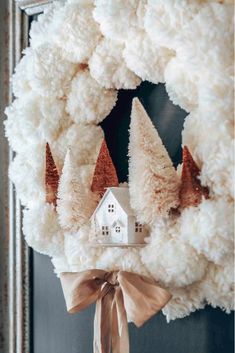 a wreath with white pom poms and a house on top is hanging from the front door