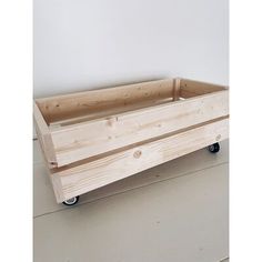 a wooden box sitting on top of a floor next to a white wall and black wheels