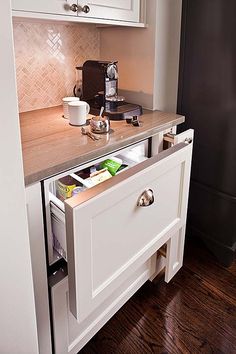 an open drawer in the middle of a kitchen counter with white cabinets and drawers on each side