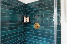 a shower with blue tiles and gold fixtures in the shower head is next to a white toilet