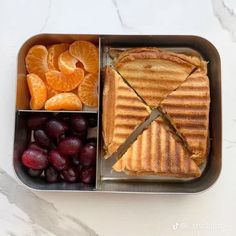 a lunch box with fruit, sandwich and crackers in it on a marble table