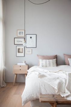 a white bed sitting next to a wooden table with pictures on the wall above it