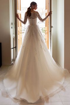 a woman standing in front of a doorway wearing a wedding dress with long sleeves and beadings