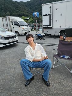 a man sitting in a chair next to other cars and trucks on a lot with mountains in the background