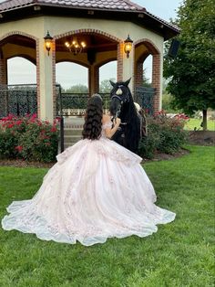 a woman in a wedding dress sitting next to a horse on the grass near a gazebo