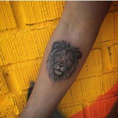 a lion tattoo on the left forearm and arm, with an orange brick wall in the background