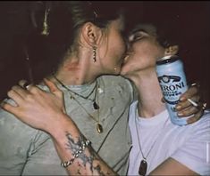 two people kissing each other while one holds a can of beer in front of their face