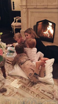 a woman and two children sitting on the floor in front of a fire place