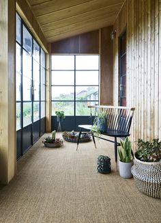 a room with wooden walls and plants on the floor, along with two large windows