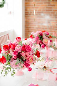 a table topped with pink and red flowers on top of a white table covered in plates