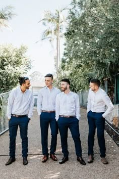 three men standing next to each other in front of trees and bushes, one is wearing a white shirt and the other has dark blue pants