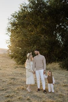 a man and woman holding hands while standing next to a small child in a field