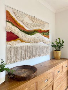 a wall hanging on the side of a wooden dresser next to a potted plant