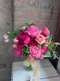 a bouquet of pink flowers sitting on top of a white table next to a brick wall