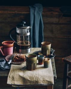 a table topped with cups and plates filled with food next to a coffee pot on top of a wooden table