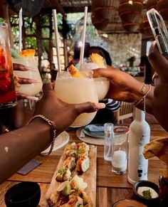 people holding up drinks at a table with plates and bowls on the table in front of them