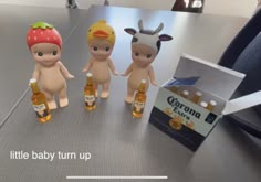 three little baby dolls sitting next to bottles of beer on a table with an open box