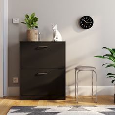 a black filing cabinet with two drawers and a clock on the wall above it next to a plant