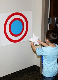 a young boy holding up a paper star next to a wall with a target on it