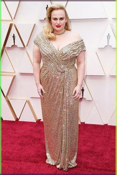 a woman in a gold gown on the red carpet at an oscars event with her hands behind her back