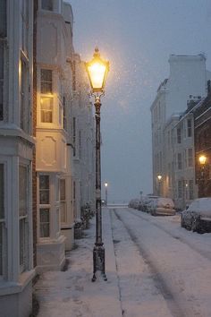 a street light in the middle of a snow covered road with buildings on both sides