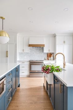 a kitchen with white and blue cabinets, an island countertop and gold pendant lights