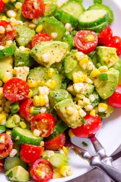 a white plate topped with cucumber, corn and tomato salad next to a fork