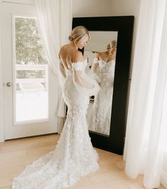 a woman standing in front of a mirror wearing a wedding dress