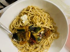 a white bowl filled with pasta and vegetables on top of a table next to utensils